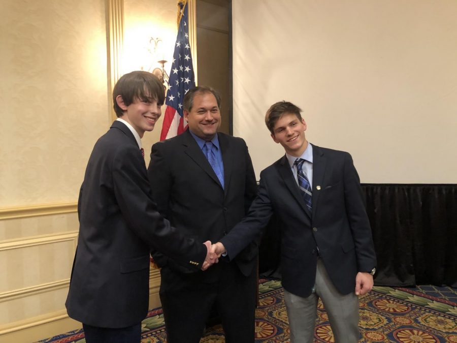Cass Rutledge (L) and Alex Stradinger (R), the incoming and outgoing Youth Legislature governors, shake hands with Mr. Christopher Lay (center), the program's director.